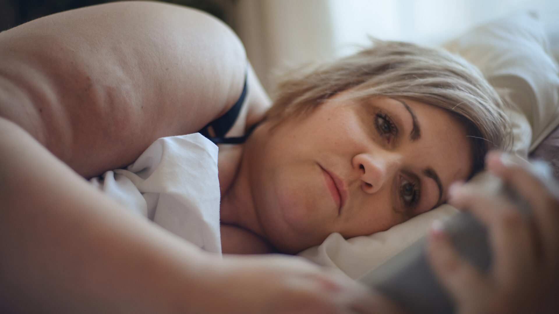 Femme obèse isolée socialement regardant son téléphone dans son lit